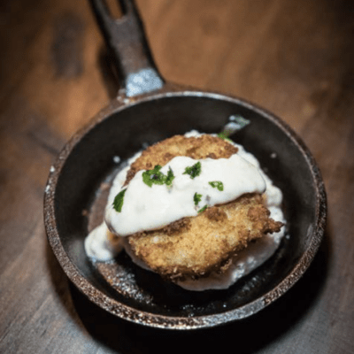 A fried green tomato on a biscuit in a small cast iron with a white remoulade on top