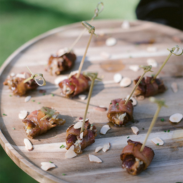 Bacon wrapped bacon with a skewer with sliced almonds on a wooden circle tray