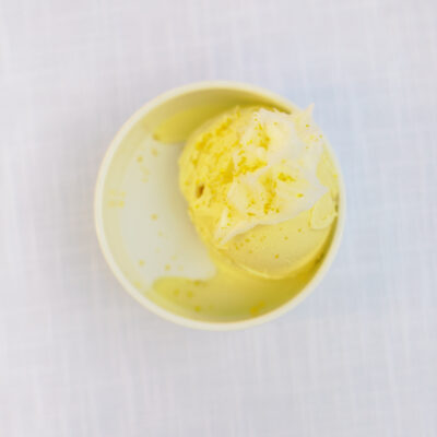 A single scoop of ice cream in a small white dish on a white textured background