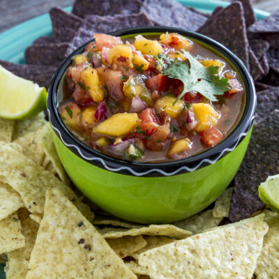 peach salsa in a green bowl with blue and white chips on a blue plate
