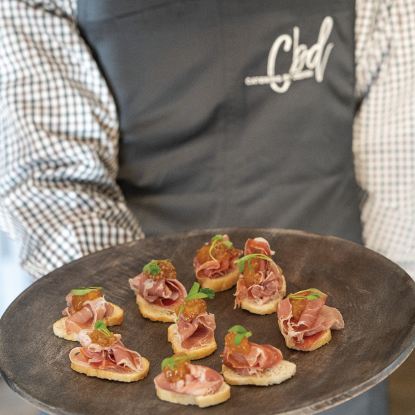 A worker in CBD uniform holding a tray of crostinis with proscuitto