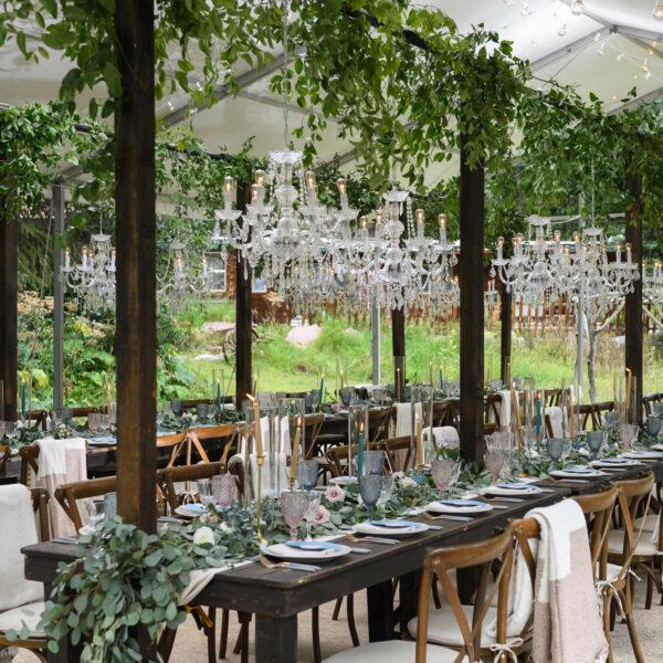 Large wood tables with lots of greenery and chandeliers