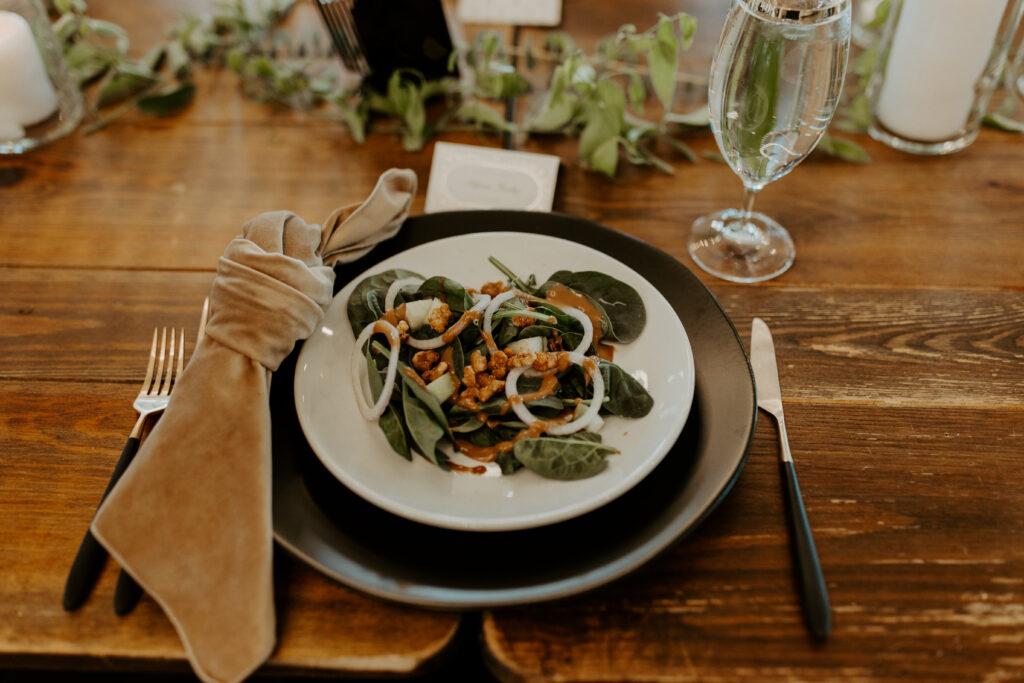 A spinach salad with onion on a white plate on a wooden table with black and gold silverware