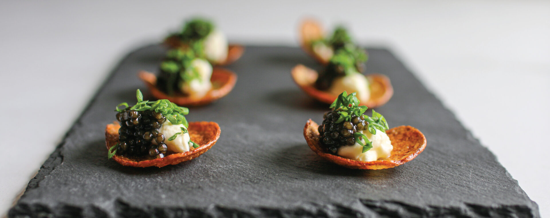 A fried red potato chip on a black slate serving platter topped with creme fraiche and caviar.