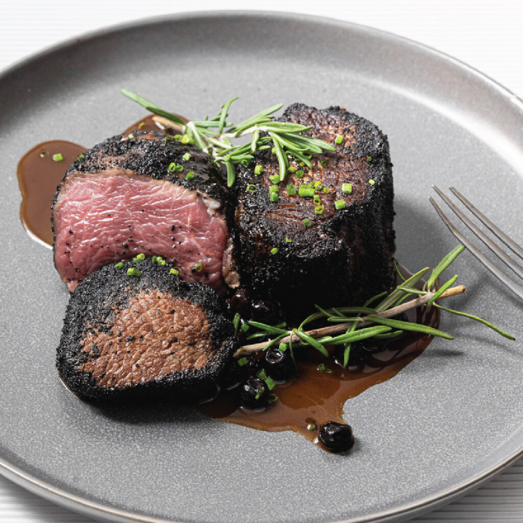 Beef Tenderloin rubbed with coffee and sliced on a plate with herbs.