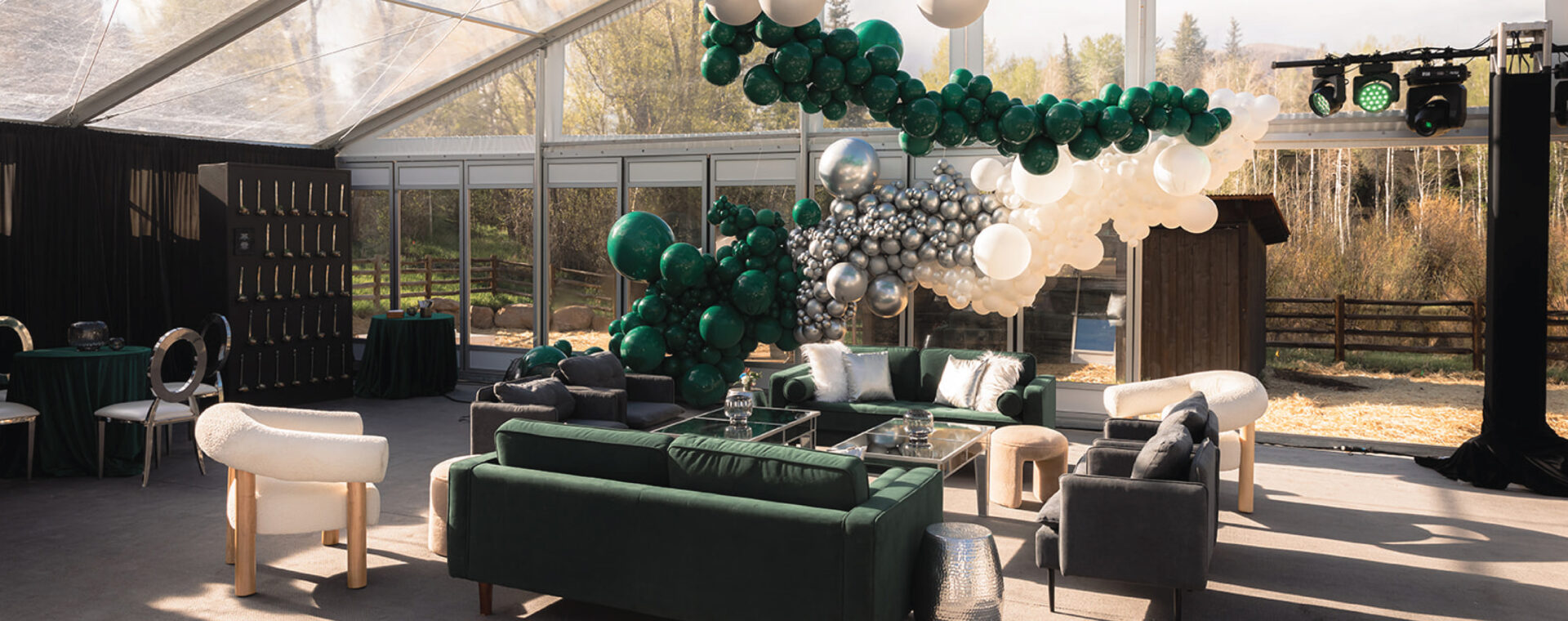 Dark green lounge furniture in a tent with green, silver and cream balloons in the background.