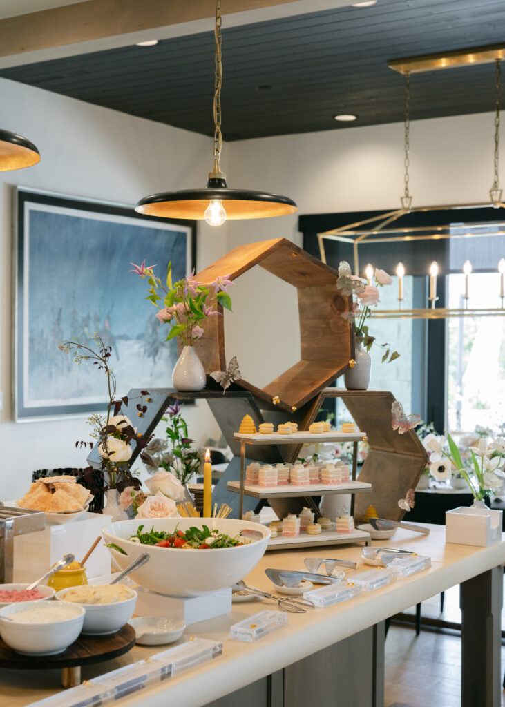 Buffet setting with honeycomb shaped shelves, a three tier tray with desserts, large salad bowl, etc.