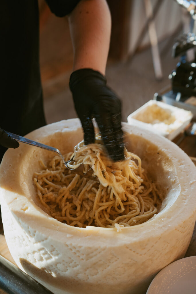 Chef tossing fresh pasta inside a Parmesan cheese wheel at an interactive catering station.