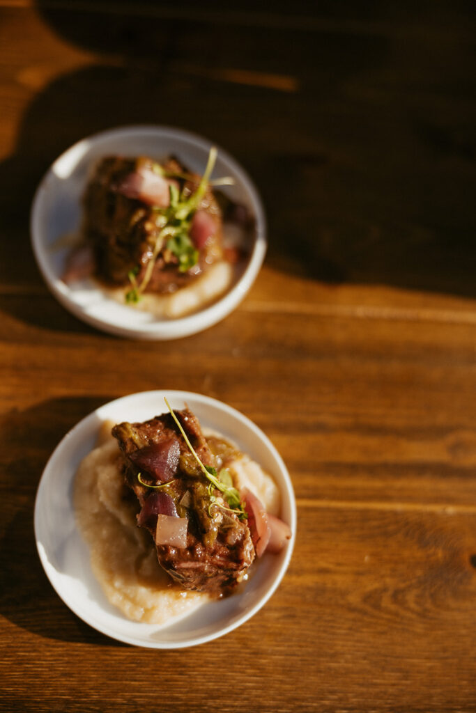 Two beautifully plated beef entrées served with creamy mashed potatoes on a wooden table.