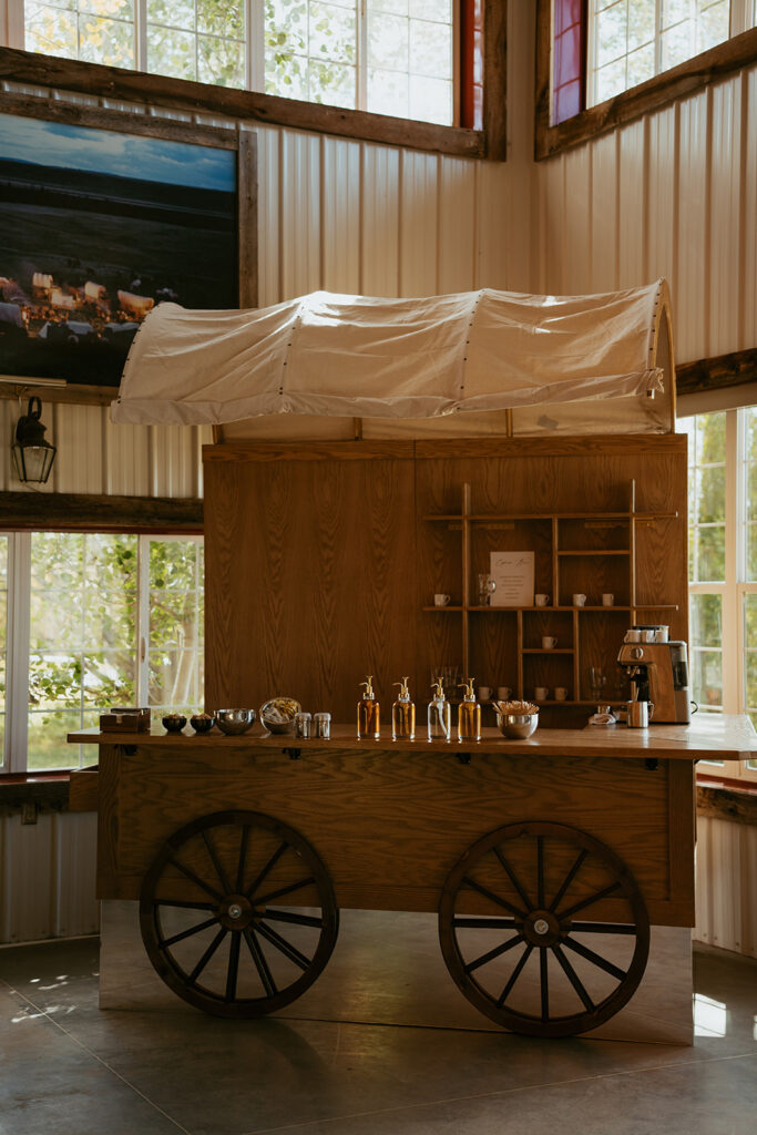 Rustic wooden wagon bar with custom shelving inside an elegant barn wedding venue.